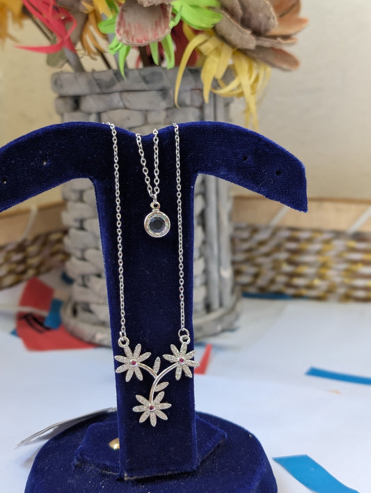 Silver necklace with floral design on a blue stand with a blurred background